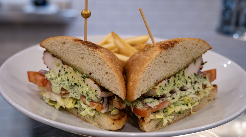 Sandwich cut in half on white plate. Toothpick on each half. Open part of sandwich towards camera so we can see inside.