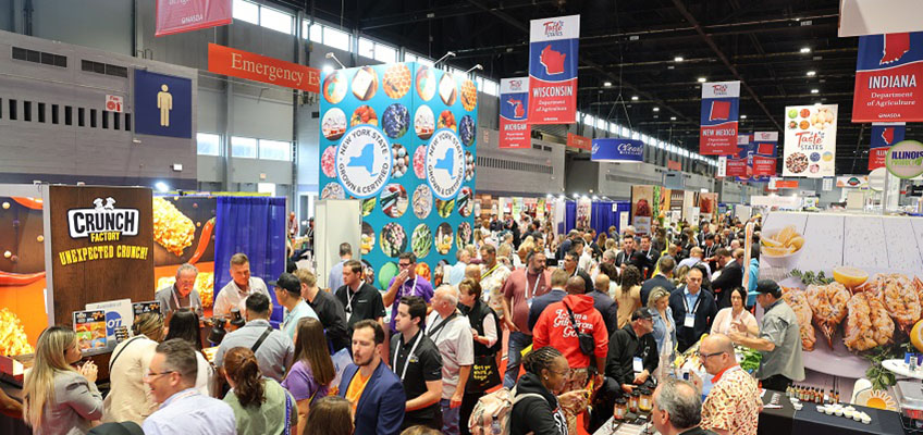 The show floor at the 2025 National Restaurant Show. Pictured is a crowd of people surrounded by colorful signage. Visible is folks tasting food