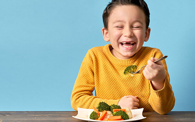 Young boy eating plate of veggies and grinning - Kids LiveWell
